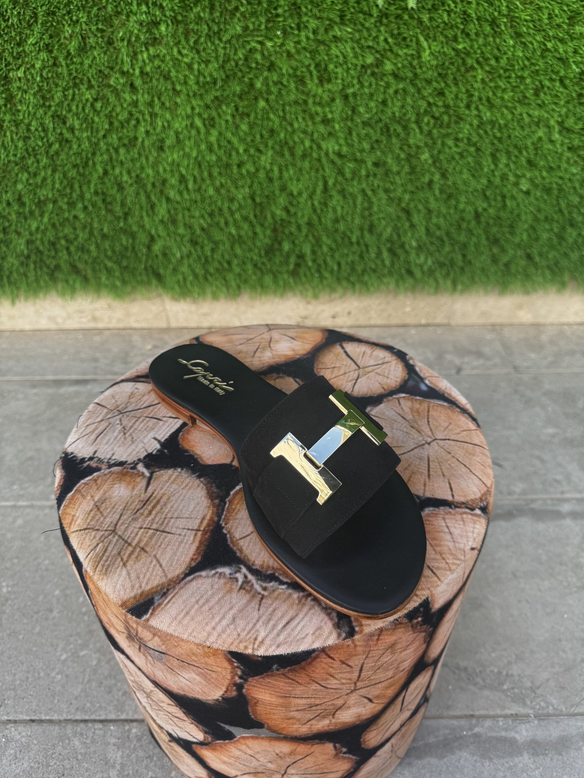 Capri T slider — 3/4 angle on wood pouf, Italian black suede with gold T-bar ornament — Capri Bells Capri Summer Edition